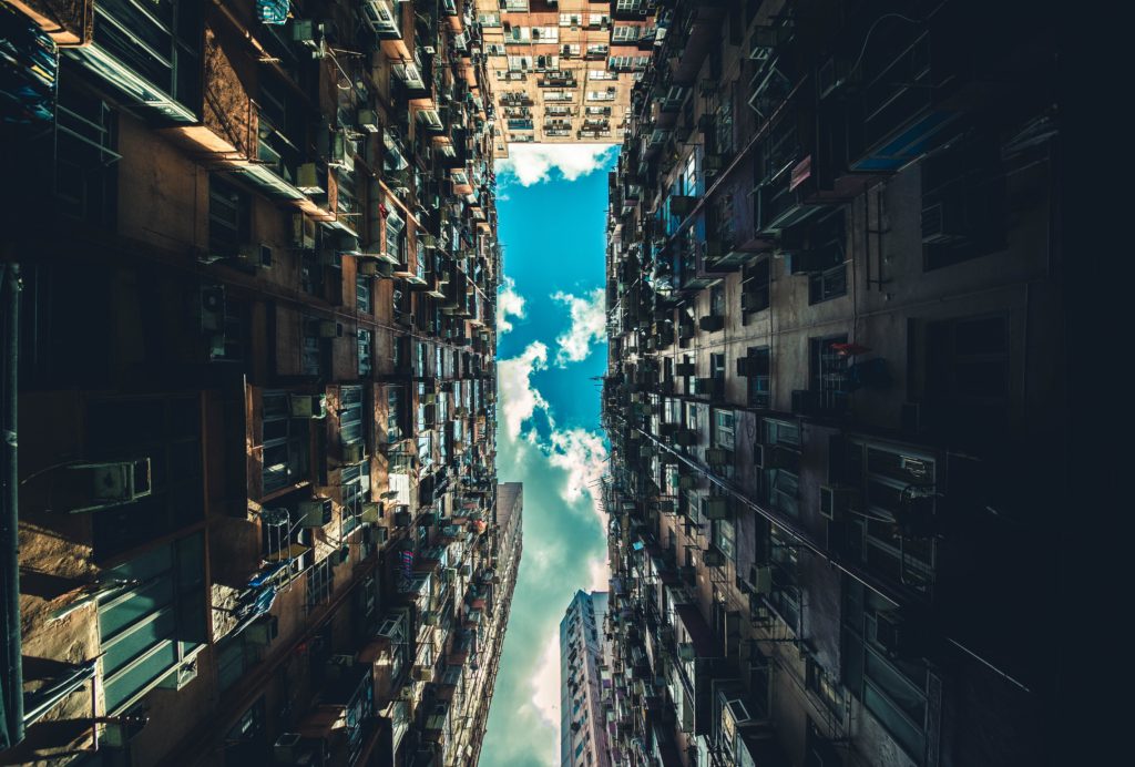 view of a blue sky with sun lit clouds looking up from an ally between buildings creating a long perspective reminiscent of eternity