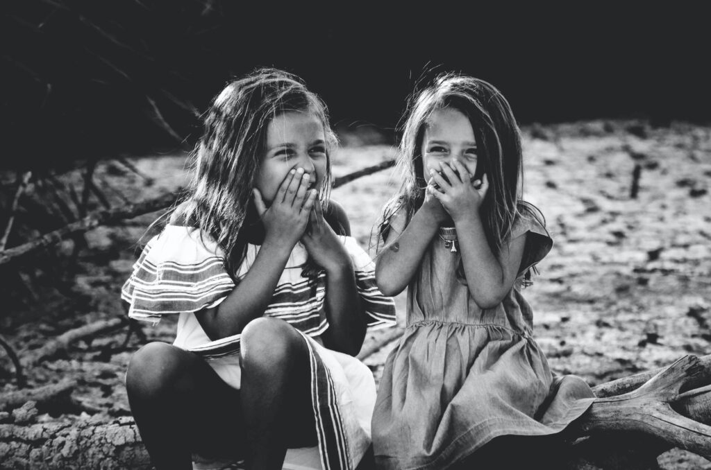 two little girls sitting together sharing a laugh as they cover their mouths to try and hold it in